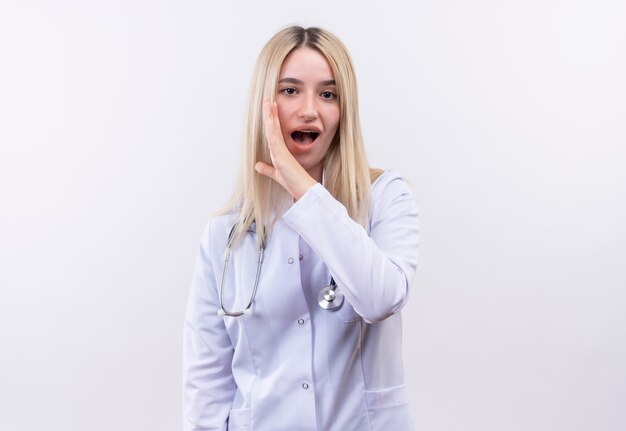 jovem loira de médico usando estetoscópio e bata médica com aparelho dentário sussurra na parede branca isolada