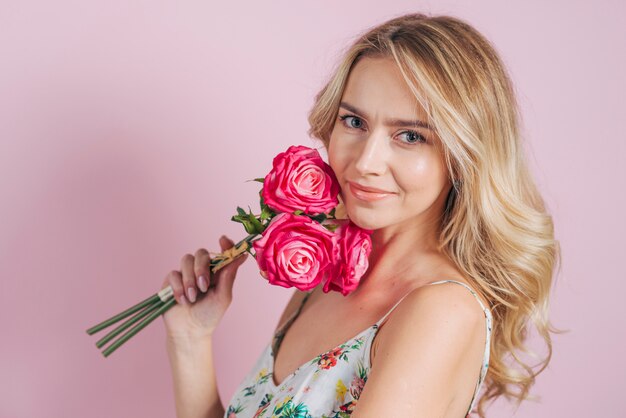 Jovem loira segurando rosas na mão contra fundo rosa