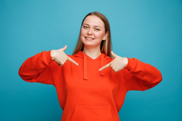 Jovem loira sorridente apontando para si mesma