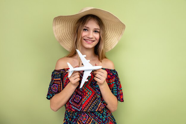 Jovem loira sorridente com chapéu de sol segurando o modelo do avião