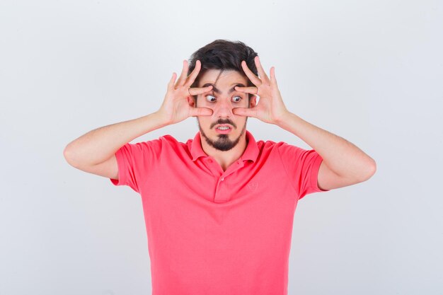 Jovem macho abrindo os olhos com as mãos na camiseta rosa e parecendo ansioso. vista frontal.