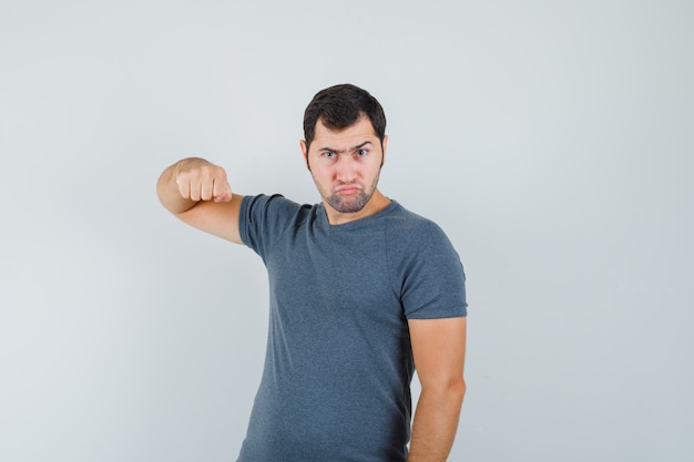 Jovem macho ameaçando com o punho em uma camiseta cinza e parecendo nervoso