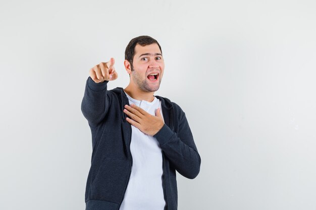 Jovem macho apontando para a câmera em t-shirt, jaqueta e olhando alegre. vista frontal.