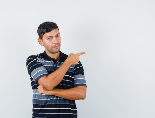 Jovem macho apontando para o lado em t-shirt e olhando com certeza. vista frontal.