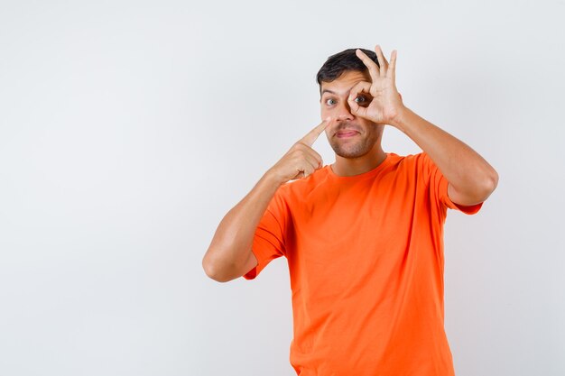 Jovem macho apontando para ok assinar no olho em camiseta laranja