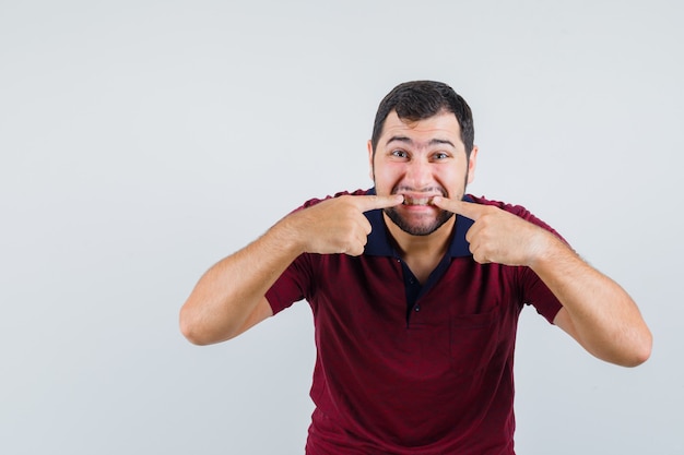 Jovem macho apontando para os dentes em uma camiseta vermelha, vista frontal.