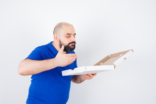 Foto grátis jovem macho cheirando a caixa de pizza aberta em t-shirt e olhando encantado, vista frontal.