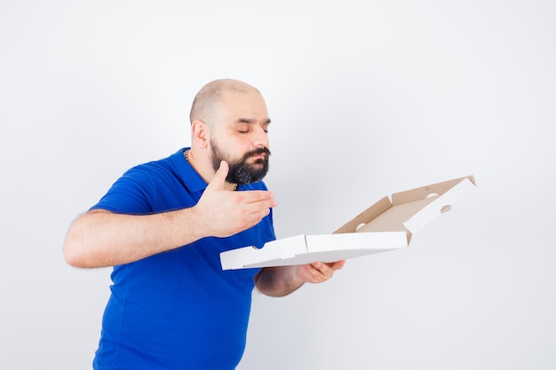 Jovem macho cheirando a caixa de pizza aberta em t-shirt e olhando encantado, vista frontal.