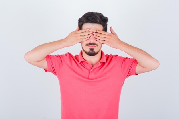 Jovem macho cobrindo os olhos com a mão na camiseta e bonito. vista frontal.