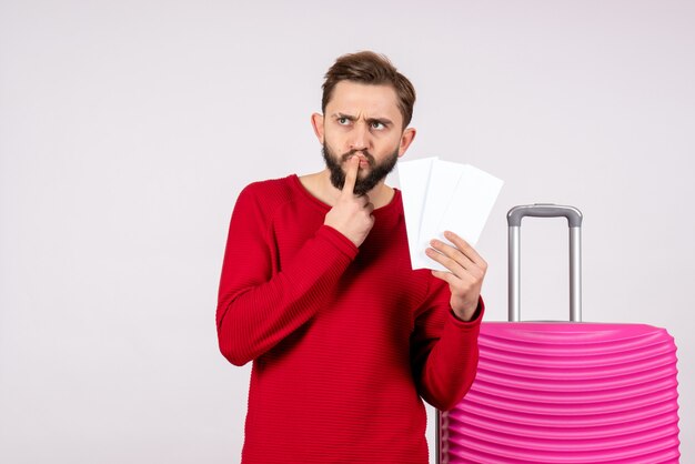 Jovem macho com bolsa rosa segurando passagens de avião na parede branca. Viagem voos viagem férias emoção foto turística