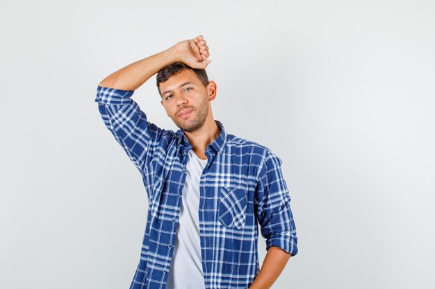 Jovem macho com camisa, inclinando a cabeça no braço levantado e olhando bonito, vista frontal.