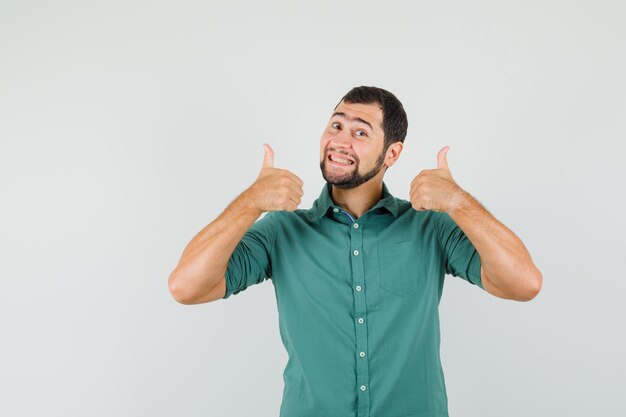 Jovem macho com camisa verde aparecendo o polegar e parecendo feliz, vista frontal.