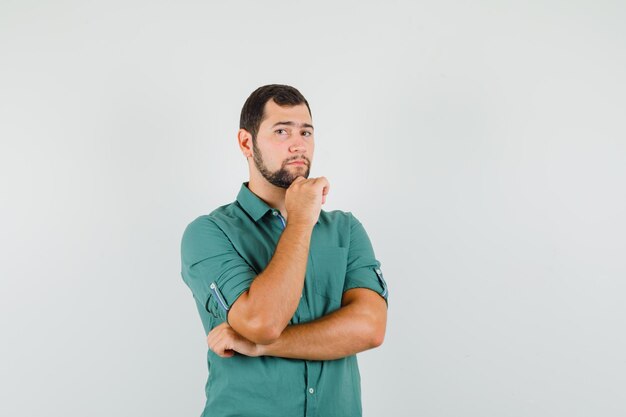 Jovem macho com camisa verde em pé e olhando atenta, vista frontal.