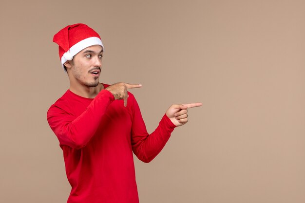 Jovem macho com capa de natal no fundo marrom emoção feriado de natal