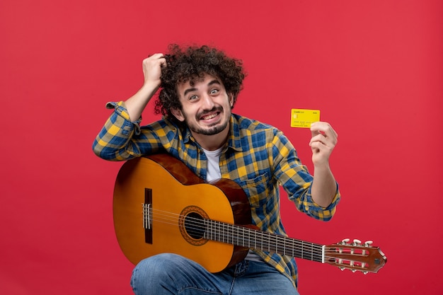 Jovem macho com guitarra, segurando o cartão do banco na cor vermelha, performance músico show ao vivo banda dinheiro