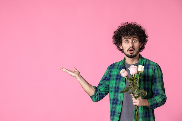 Foto grátis jovem macho com rosas cor de rosa na frente