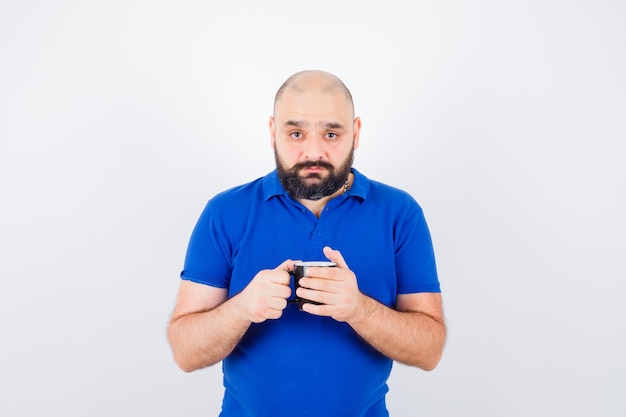 Foto grátis jovem macho de camisa azul, segurando o copo, vista frontal.