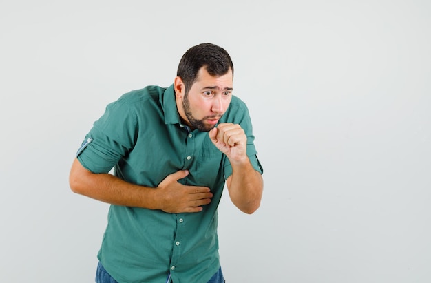 Jovem macho de camisa verde, tossindo e parecendo desconfortável, vista frontal.