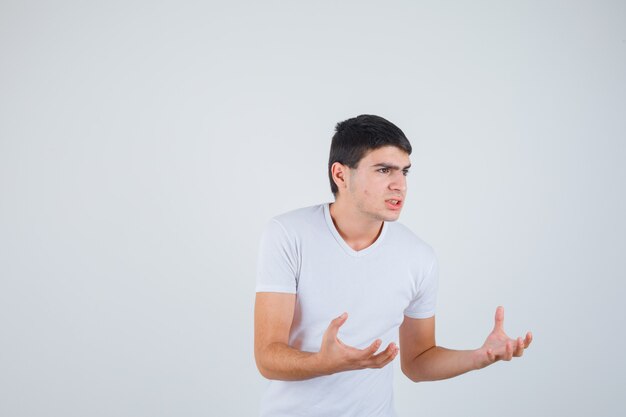 Jovem macho de mãos dadas para pegar algo na t-shirt e olhar sério. vista frontal.