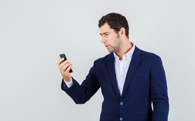 Jovem macho de terno olhando para o smartphone e olhando sério, vista frontal.