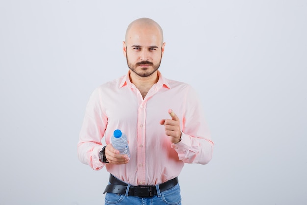 Jovem macho em camisa, jeans apontando a câmera e olhando confiante, vista frontal.