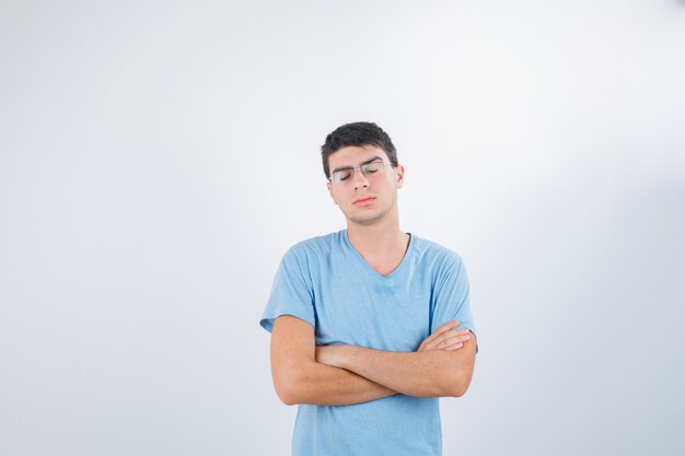 Jovem macho em pé com os braços cruzados na camiseta e parecendo desapontado, vista frontal.