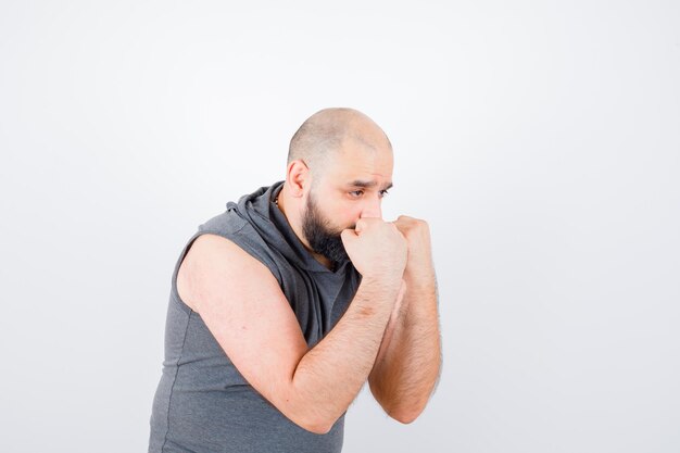 Jovem macho em pose de defesa com capuz sem mangas e parecendo confiante, vista frontal.