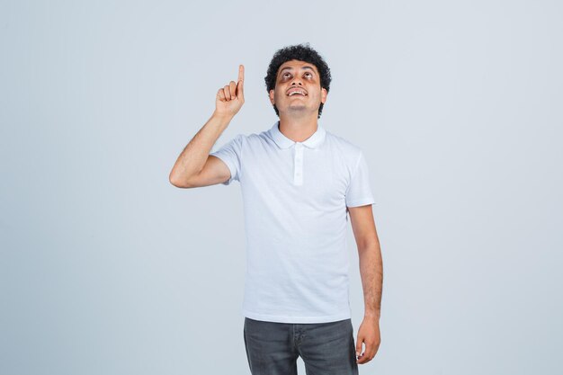 Jovem macho em t-shirt branca, calça apontando para cima e olhando agradecido, vista frontal.