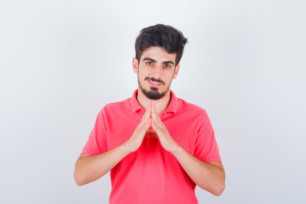 Jovem macho em t-shirt fazendo gesto de telhado de casa e olhando bonito, vista frontal.