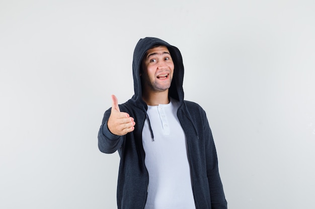 Jovem macho em t-shirt, jaqueta dando a mão para apertar e olhar alegre, vista frontal.