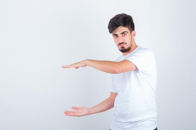 Jovem macho em t-shirt mostrando sinal de tamanho e olhando confiante, vista frontal.