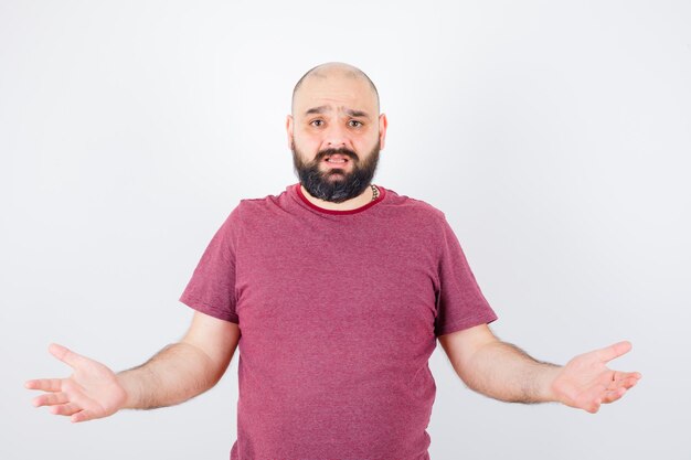 Jovem macho em t-shirt rosa, mostrando um gesto de impotência e olhando descontente, vista frontal.