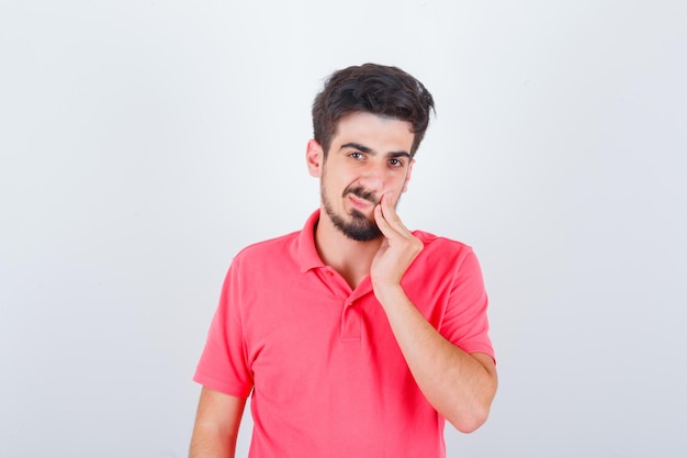Jovem macho em t-shirt rosa tendo dor de dente e olhando pensativo, vista frontal.