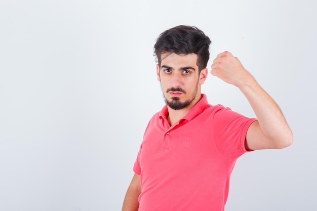 Jovem macho em uma camiseta rosa, mostrando o punho cerrado e parecendo confiante, vista frontal.