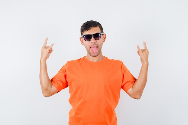 Foto grátis jovem macho fazendo o símbolo do rock enquanto mostra a língua em uma camiseta laranja e parece louco