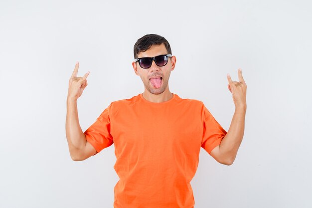 Jovem macho fazendo o símbolo do rock enquanto mostra a língua em uma camiseta laranja e parece louco