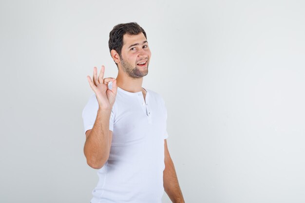 Jovem macho fazendo sinal de ok e sorrindo em uma camiseta branca