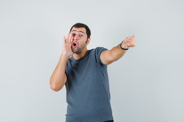 Jovem macho gritando enquanto aponta para longe na vista frontal de t-shirt cinza.