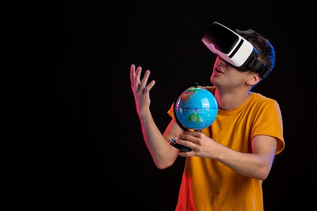 Foto grátis jovem macho jogando realidade virtual segurando um globo na superfície escura