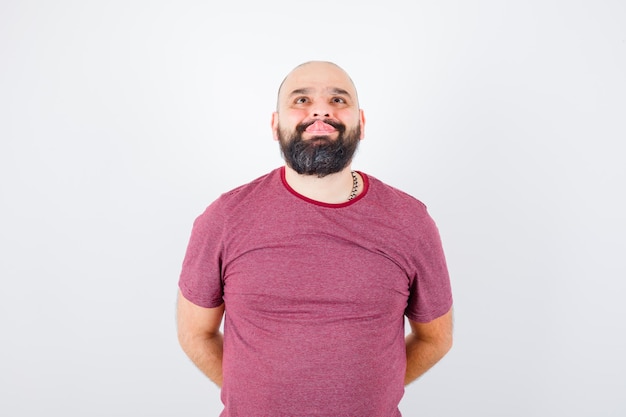 Jovem macho mostrando a língua enquanto olha para cima em uma camiseta rosa e parece estranho. vista frontal.