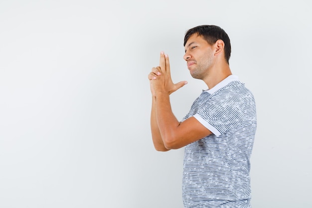 Jovem macho mostrando gesto de arma em t-shirt e parecendo confiante. .