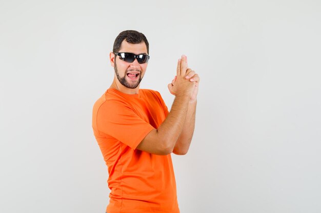 Jovem macho mostrando gesto de arma em t-shirt laranja e parecendo confiante. vista frontal.