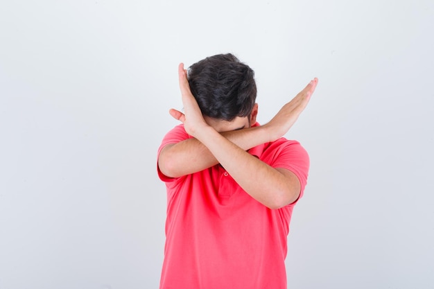 Jovem macho mostrando o gesto de parada em t-shirt e olhando com medo, vista frontal.