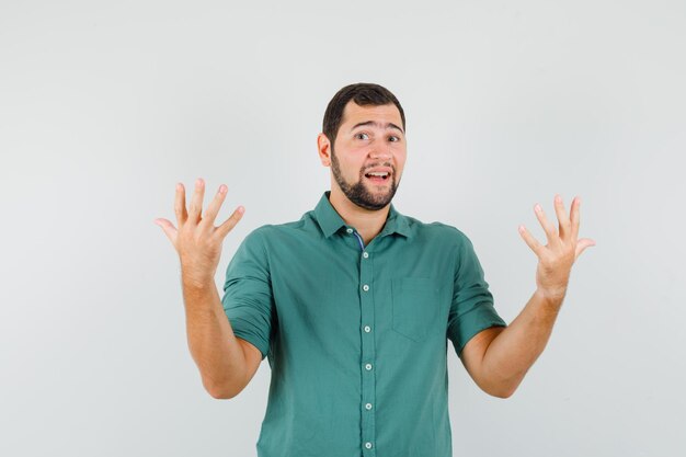 Jovem macho mostrando-se indefeso com uma camisa verde e parecendo desesperado. vista frontal.