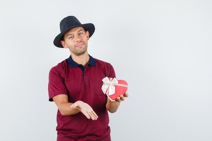 Foto grátis jovem macho mostrando seu dom de camisa vermelha e parecendo feliz. vista frontal. espaço para texto
