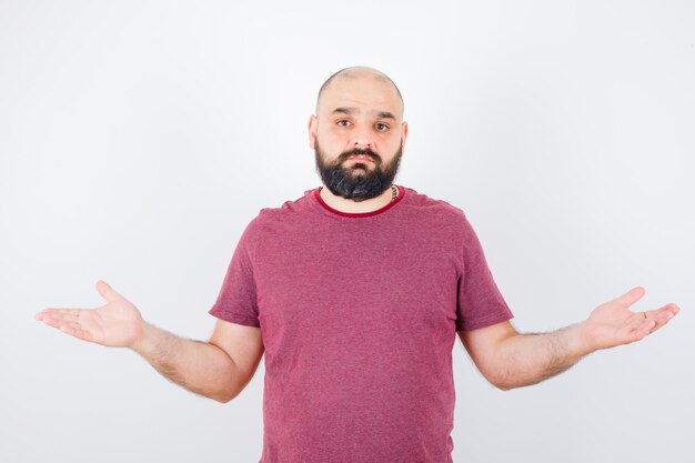 Jovem macho mostrando um gesto desamparado em uma camiseta rosa e parecendo descontente. vista frontal.