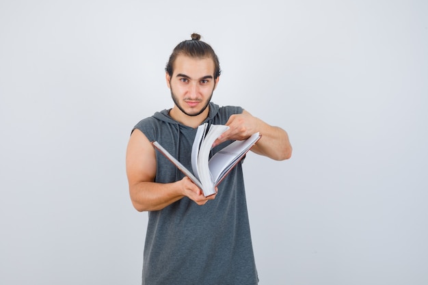 Jovem macho olha através do livro com capuz sem mangas e parece confiante. vista frontal.