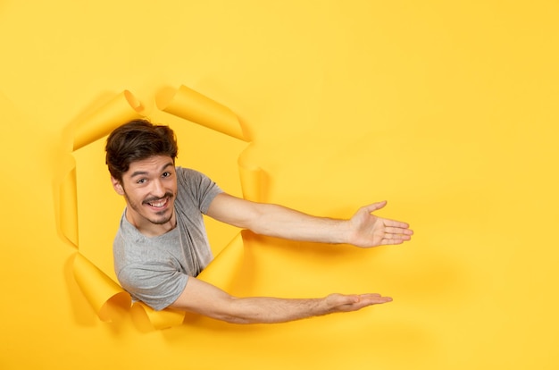 Jovem macho olhando de fundo de papel amarelo rasgado venda facial de cara interna