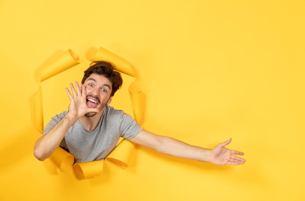 Jovem macho olhando de uma superfície de papel amarelo rasgado