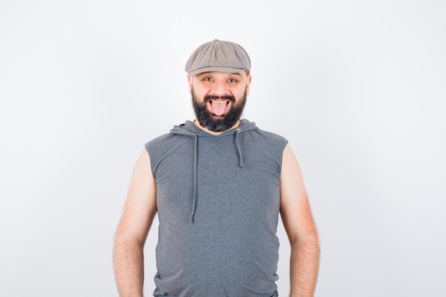 Jovem macho olhando para a câmera com capuz sem mangas, boné e parecendo alegre. vista frontal.